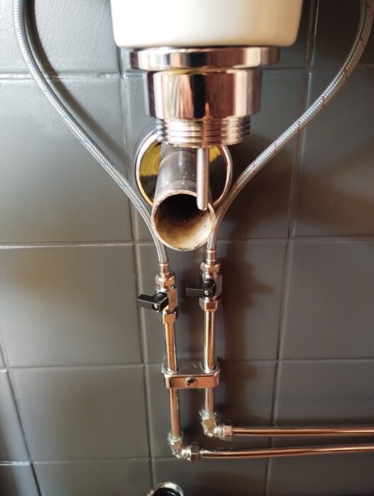 Avloppsrör och vattenlås under handfat, ocentrerat och anslutet till väggen med specialböj. Problem med tätning vid installation.