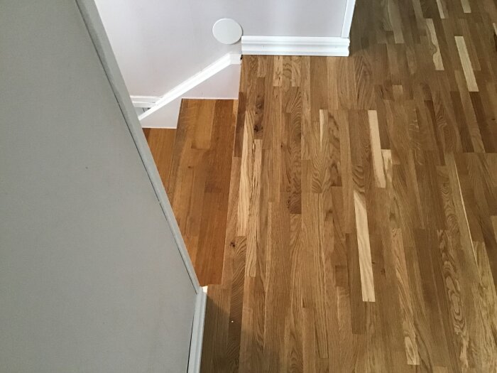 Parkettgolv på övervåning framför trappa, svårigheter med lister kring trappans vinklar.