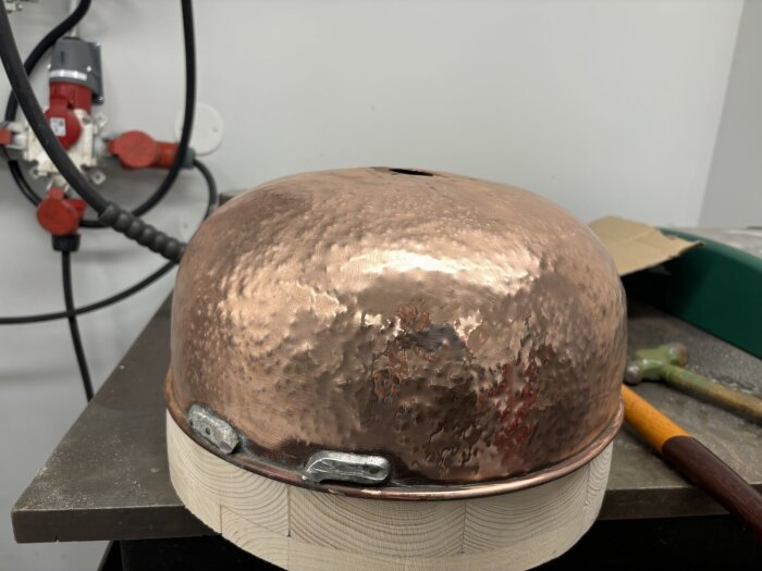 Handslagen och polerad kopparbunke, tidigare använd som taklampa, fotograferad på verkstad med hammare i bakgrunden.