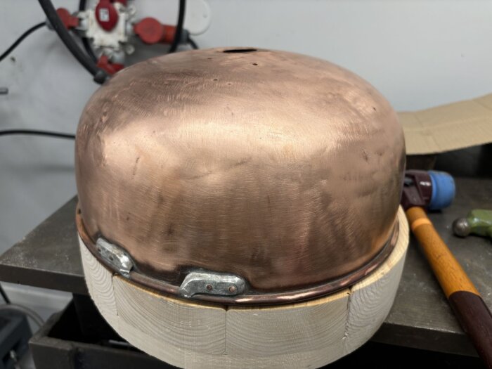 Hamrad och polerad kopparbunke som används för isolering runt skorstensrör, med träbas vid utformning.