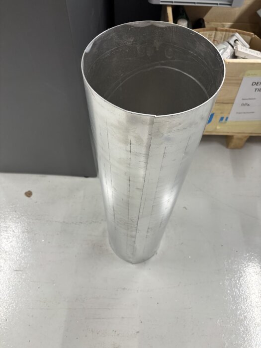 Aluminiumrör på ett golv, del av en DIY-byggprocess för skorsten. Rör vertikalt med synliga markeringar, omgiven av verktyg och material i bakgrunden.