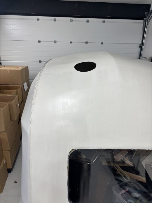 Hål i tak för skorstensgenomföring i ett vitt aluminiumfordon, fotograferat i ett garage med flyttkartonger och en synlig dörröppning i bakgrunden.