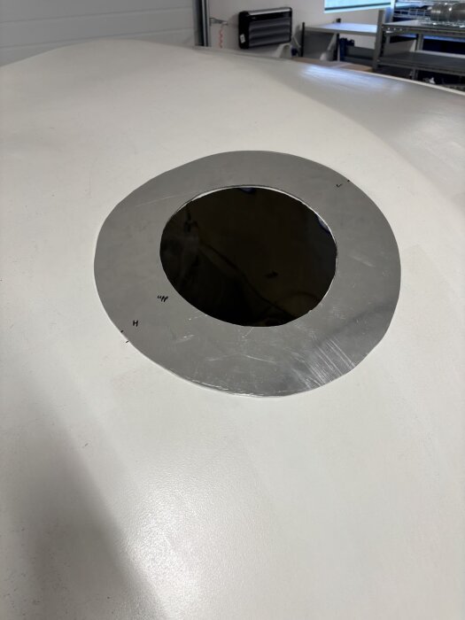 Hål i taket för skorstensrör, omgiven av ett runt metallskal. Ljus och ren arbetsmiljö synlig i bakgrunden.