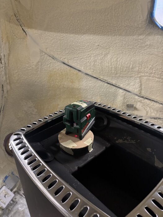 Lasermätare på montering ovanpå svart kamin inuti vagnen, förbereder exakt håltagning genom taket för skorstensinstallation.