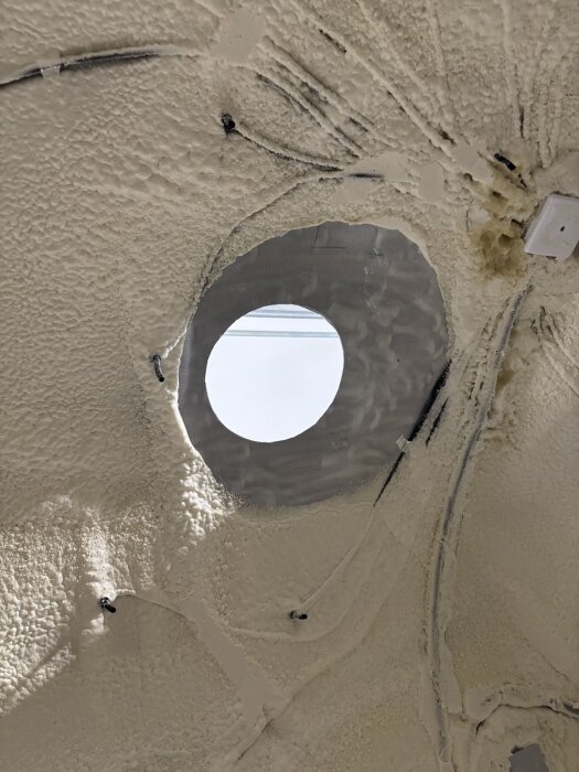 Hål i tak med material runtom, förberett för passage av skorstensrör, omgiven av isolering och tätningsmaterial.