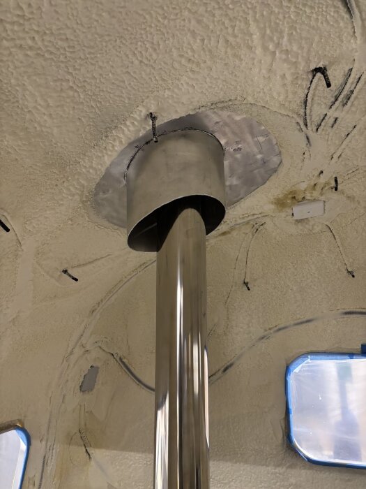 Takgenomföring med rostfritt rör och isolerad krage, monterad i taket med synlig skruv och sprayad isolering runt genomföringen.