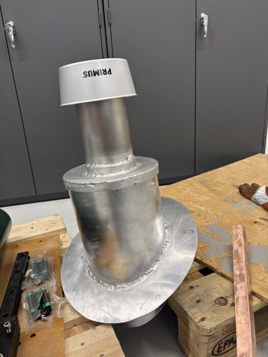 DIY regnhuv av aluminium och kastrull. Svetsade fogar synliga, placerad på träbänk i verkstad. Rustika material runtomkring.