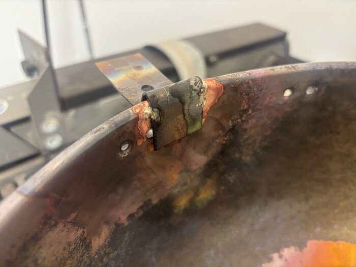 Närbild av en kastrull för stormkök med lödd fastsättning av rostfri plåtbit, del av en regnhuv för skorsten.