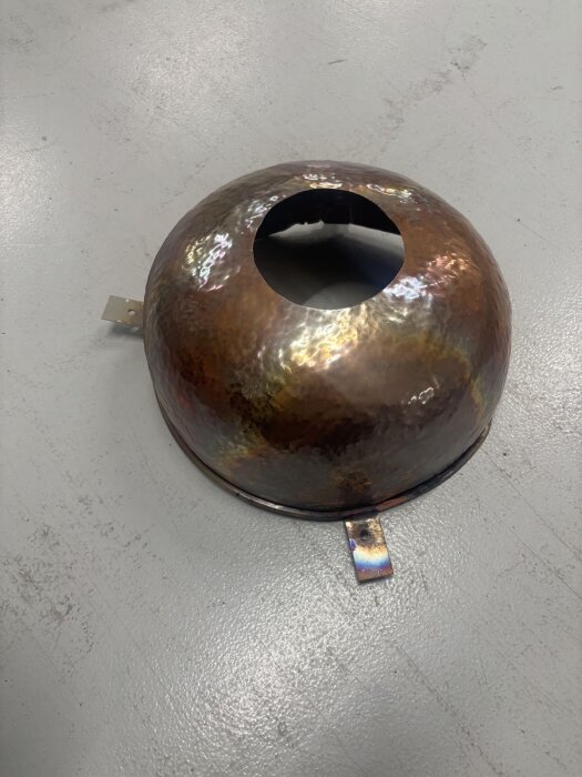 Hammrad kopparbunk modifierad med ett centralt hål och tre svetsade flikar, använd som regnhuv på skorsten i byggprojekt.