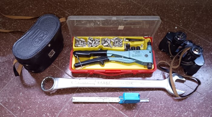 Verktyg som blindmuttertång, skiftnyckel, avståndsmätare och en rysk armékikare med fodral, liggande på golvet.