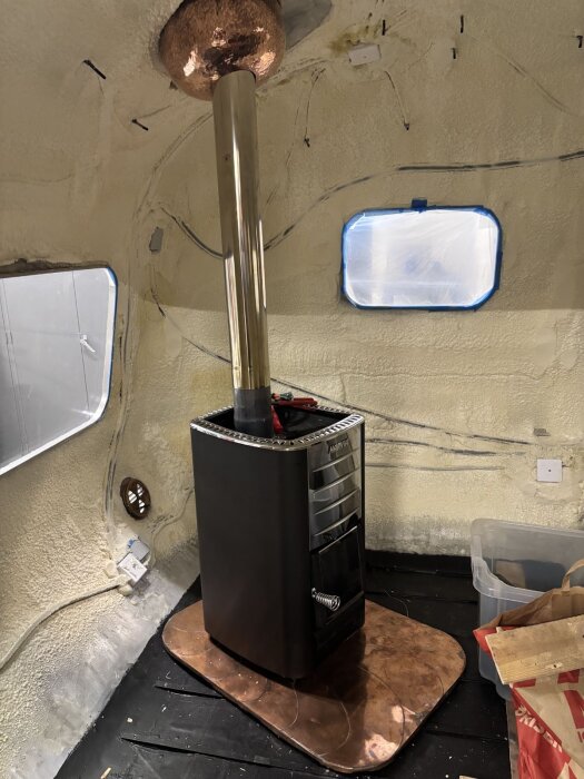 Invändig installation av en eldstad med kopparskorsten i en byggnad. Skorstenshuv och isolering syns tydligt i bilden.