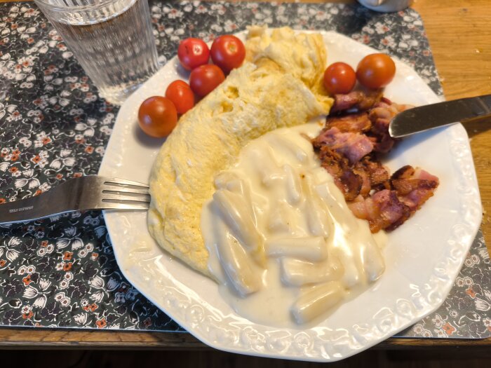 Omelett med sparrisstuvning, bacon och körsbärstomater på en tallrik, bredvid ett glas vatten.