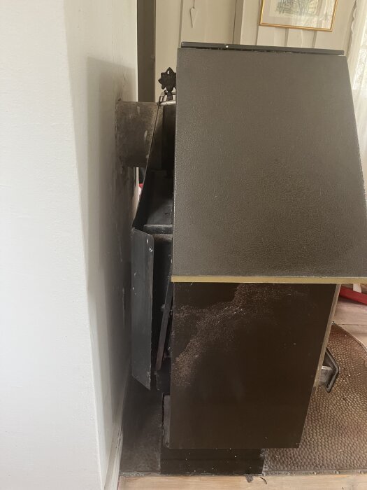 Gammal kamin ansluten till en vägg, i ett rum med trägolv, som planeras bytas ut.