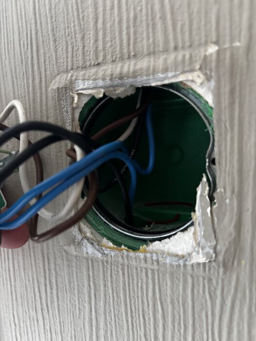 Blå, bruna och vita elkablar i ett öppnat vägguttag, visar kabeldragning i ett äldre hus byggt 1991.