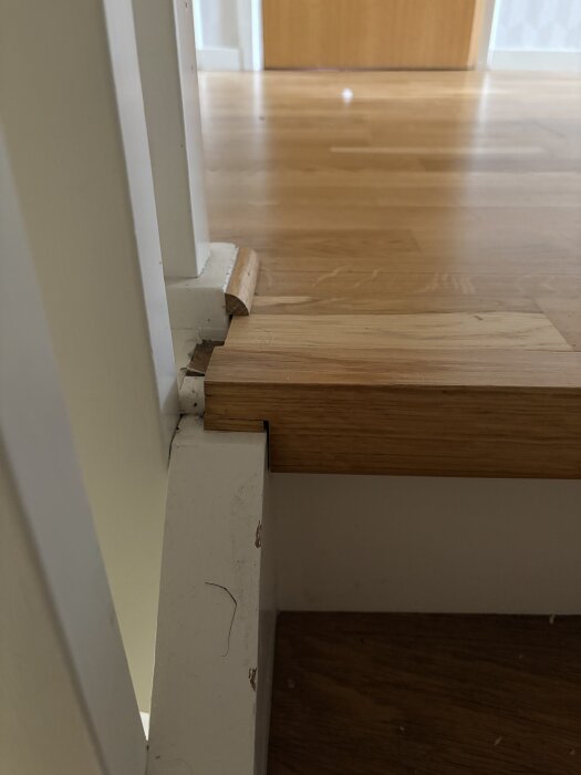 Trappnos i trä mot golv med vertikal eklist som avslut på golvlisten vid en trappa i ett hus.