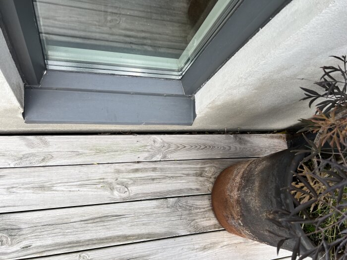 Putsad vägg och trädäck bredvid ett fönster, med en stor kruka på däcket vid väggen.