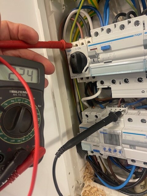 Multimeter som visar 224 VAC ansluten till kablar i en elcentral, med sonder kopplade till olika ledningar.