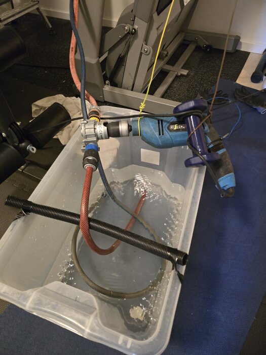 Golvvärmeslinga påfyllning; slangen är ansluten till en borrmaskin i en plastbehållare med vatten för avluftning.