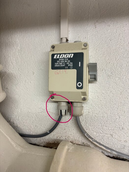 Elektrisk kopplingsdosa märkt "Eldon BAM 316" på vägg med två anslutna elledningar, med en ledning markerad med cirkel.