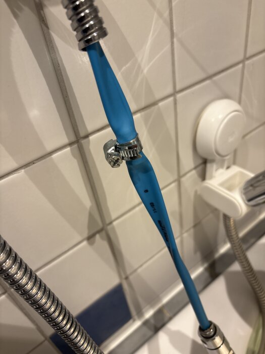 Blå tillfällig slanginstallation med metallklämma mot en vit kakelvägg.