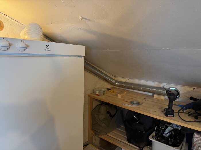 Torkskåp från Electrolux installerat i snedtak, med spirorör ut till ventilationsöppning, verktyg och hyllplan med verktyg på sidan.