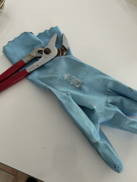 Blå handskar och en tång på ett bord. En liten glödlampa ligger på handskarna.