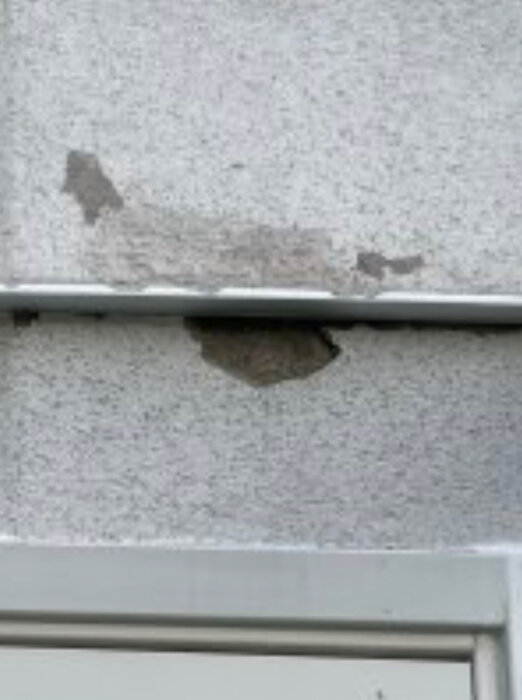 Skadad fasad på ett hus med synliga skador i ytskiktet av puts.