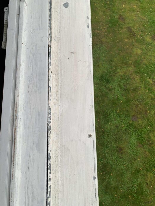 Utsikt över en sliten fönsterbräda och gräsmatta, färg flagnad, visar behov av renovering eller underhåll.