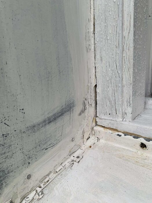 Närbild av sprucken och flagnande vit färg på en yta med vattendroppar och tecken på slitage.