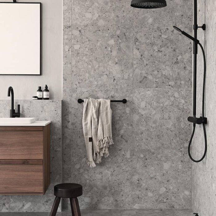 Modernt badrum med halvkaklat i ceppo di gre-kakel; handfat, spegel och dusch syns, samt en handduk på väggen.