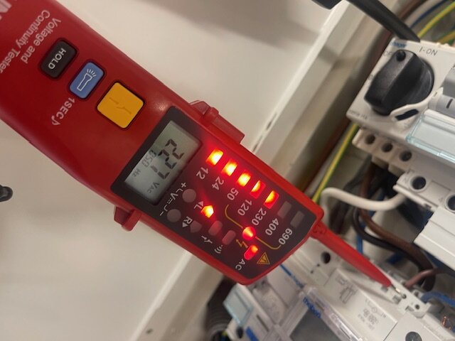 Elektriker testar strömstyrkan med en spänningsprovare, som visar 227 volt, vid installationen av en laddbox i ett garage.