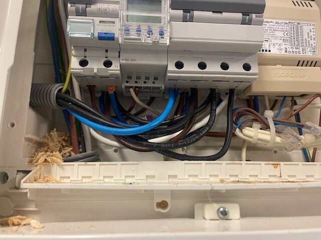 Inkoppling av laddbox i säkringsskåp, med kablar från vänster. Synliga träspån vid botten av skåpet.