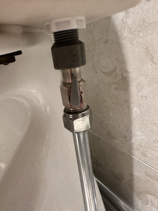 Kopplingen mellan toalett och vattenrör, med en synlig mutter och en möjlig vattenläcka.