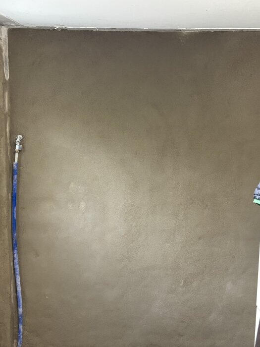 Putsad vägg med slät ytfinish och synlig blå slang på vänster sida.