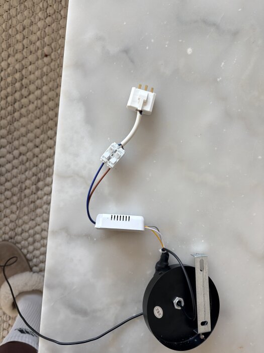 Lampans installationskomponenter med sladdar och kontakter placerade på ett bord, med en del av golvet synlig i bakgrunden.