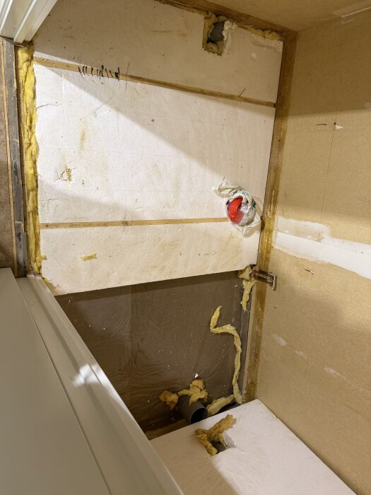 Rivningsprocess av badrumsgolv, visar borttagen golvmatta och frigolit på sandbädd med läkt. Synliga rör och isolering i golvstrukturen.