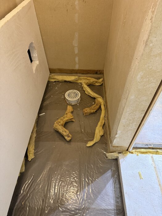 Rivet badrum med synlig golvbrunn, plastskyddad yta, frigolit och isolering spridd runt golvet.