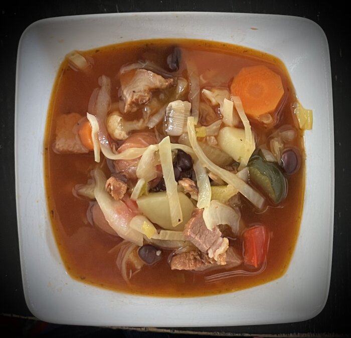 En skål med soppa innehållande köttbitar, morötter, squash, salladslök, bönor och andra grönsaker i buljong.