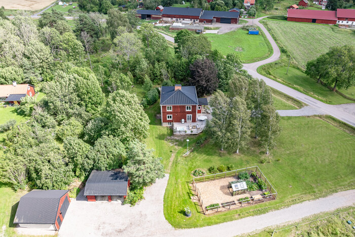 Fågelperspektiv av en lantgård med rött hus, omgivande trädgårdar och byggnader, belägen på landsbygden nära Uppsala.