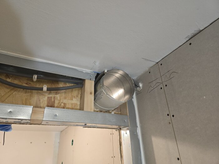 Ventilationskanal genom hål i väggen mellan OSB och gips, med flexrör ovanför. Förberedelser för isolering och vidare bygge mot vänster.