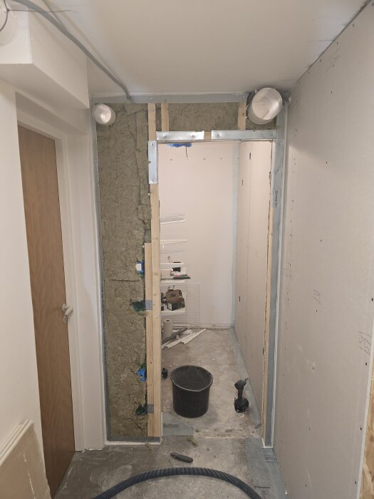 Renovering av vägg med isolering, gipsplattor och ventilationsrör i rum under konstruktion. Verktyg och material syns på golvet.