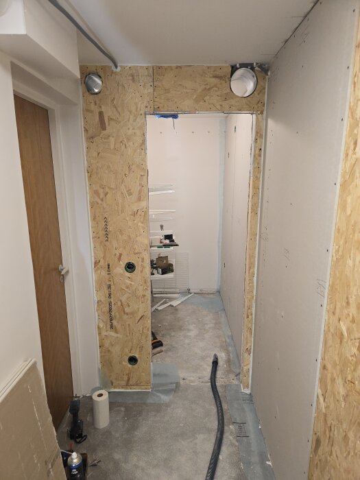 Väggkonstruktion med OSB-skivor och borrade hål för ventilationsrör, samt verktyg och material på golvet inför montering av isolering.