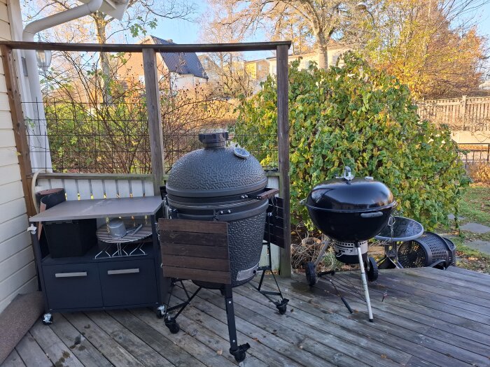Kamado och klotgrill placerade på en altan med trädgårdsbakgrund.