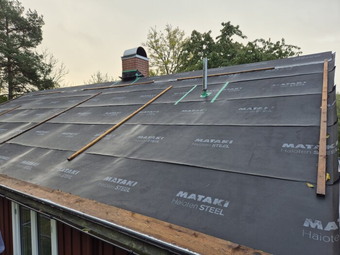 Tak med delvis fastspikad takpapp, synliga avluftningsrör och en skorsten, montering förberedd för bandtäcktplåt med duk istället för nockdalsremsa.