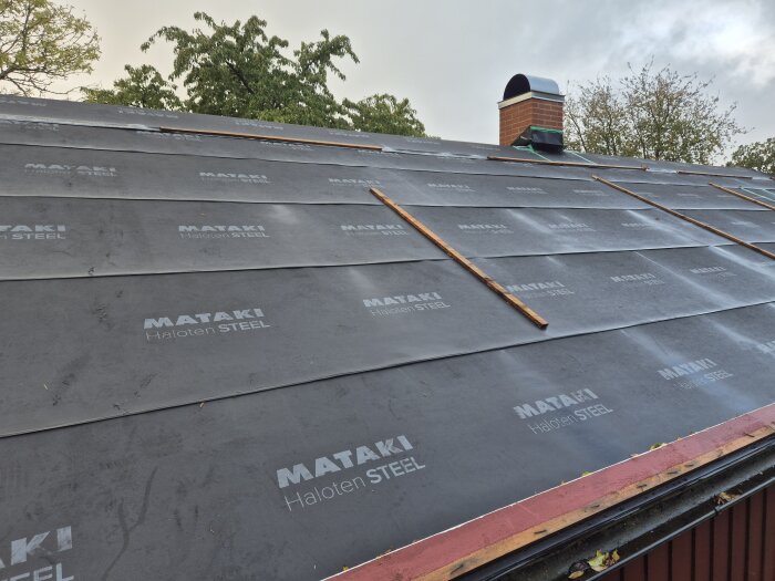 Tak med oregelbundet monterad duk, märkt "MATÄKI Haloten STEEL," otäckta nockdalsremsor och en löskant runt avluftningsrör, under frågeställning.