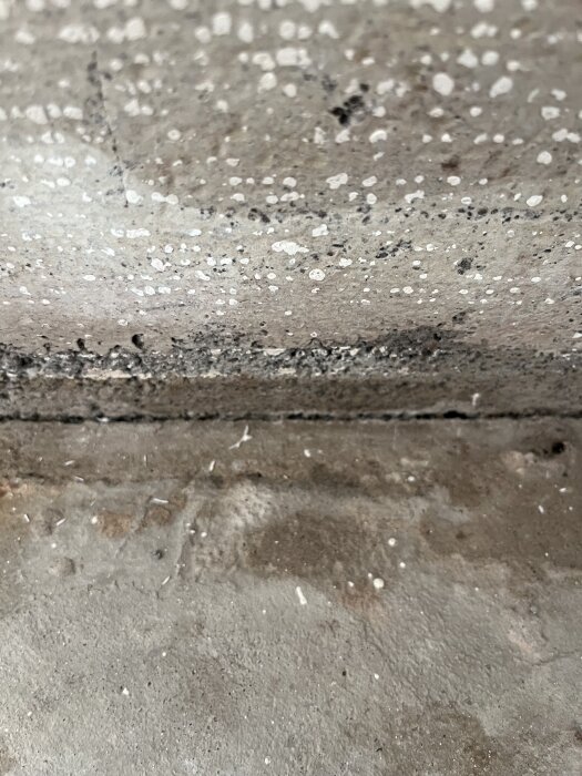 Spricka mellan golv och betongplatta med antydan till fukt.