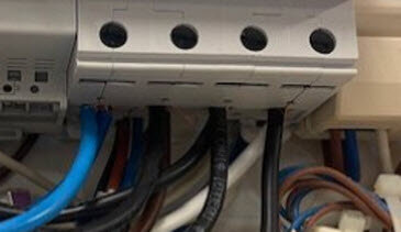 Utanpåliggande elinstallation med flera kablar, både blå och svarta, anslutna under en kopplingsenhet.