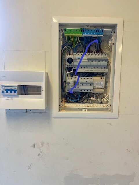 Elskåp med öppna dörrar som visar kablar, inklusive två markerade kablar i blått från ovansidan uret.