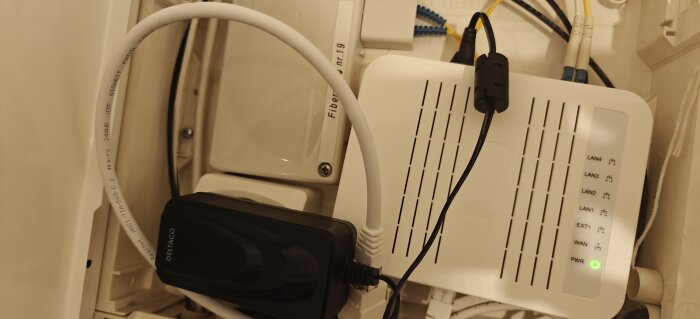 Router med anslutna kablar och LAN-indikatorer, inklusive 12V 2A strömadapter synlig, en DELTACO-enhet ansluten till nätverk.