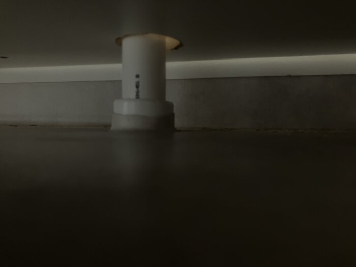 Rörgenomföring för spillvatten i badrum med våtrumsmatta uppvikt mot vit tätning runt röret.